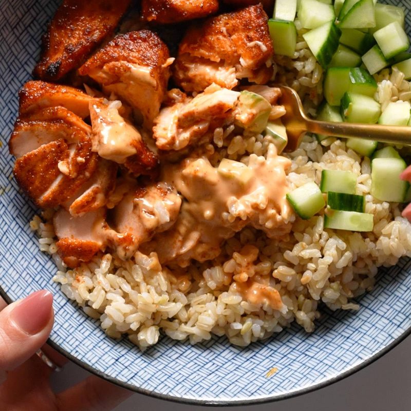 Air fryer salmon in a bowl with rice, cucumber, and sauce.