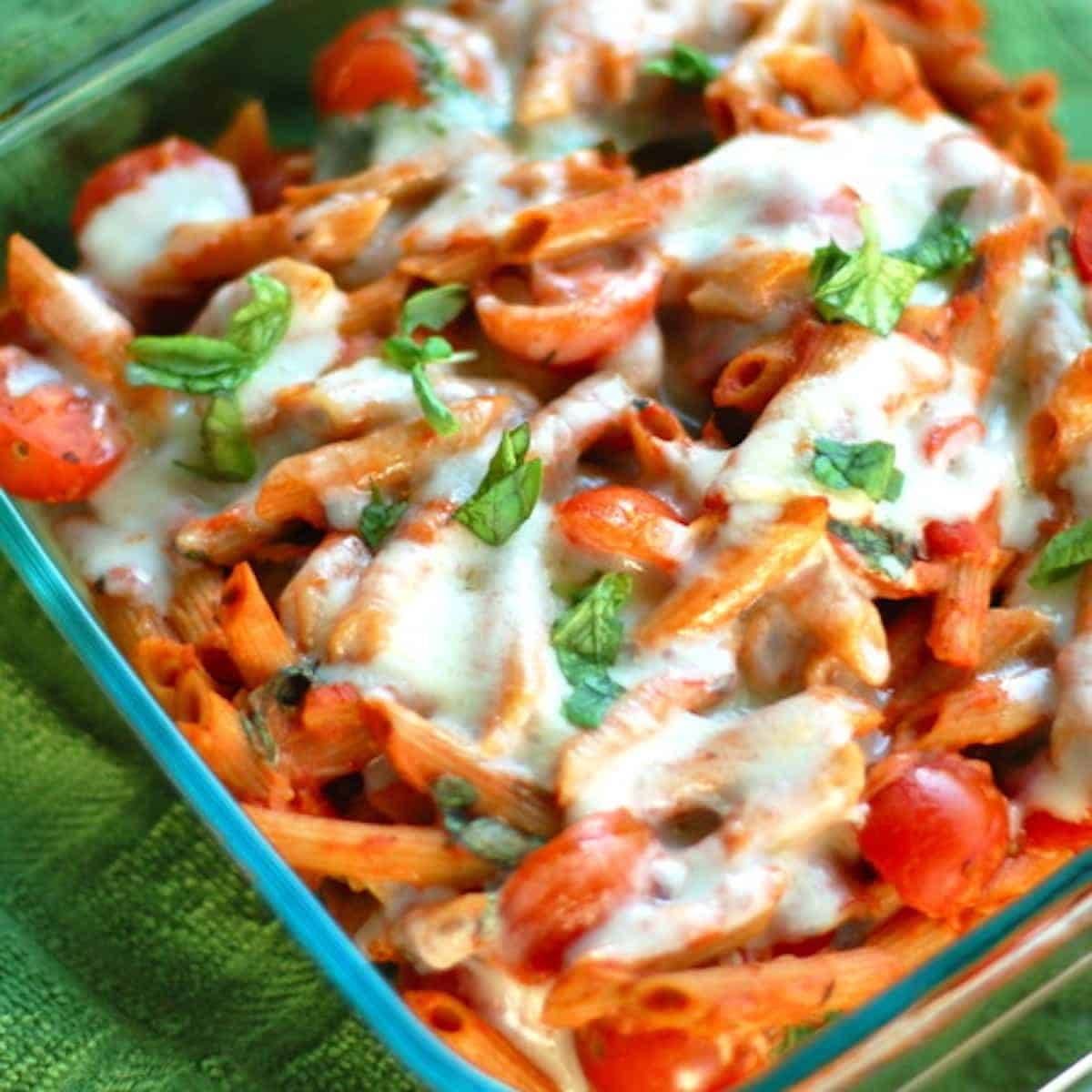 Caprese penne pasta with sweet cherry tomatoes, mozzarella, and fresh basil in a glass dish.