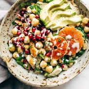 Spa salad in a bowl topped with chicken, avocado, and oranges.